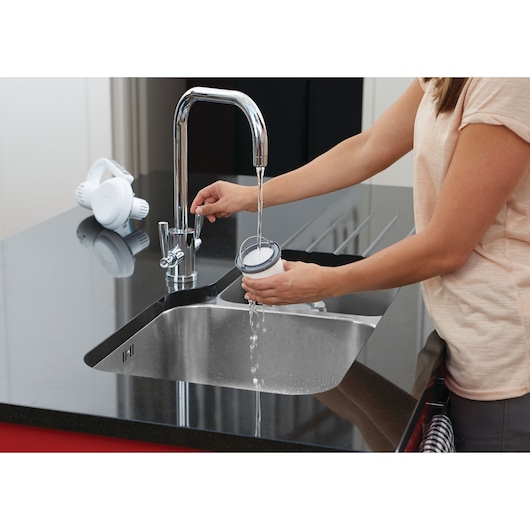 BLACKDECKER PV1820L vacuum filter being rinsed under a kitchen faucet, hand holding the filter above a sink.