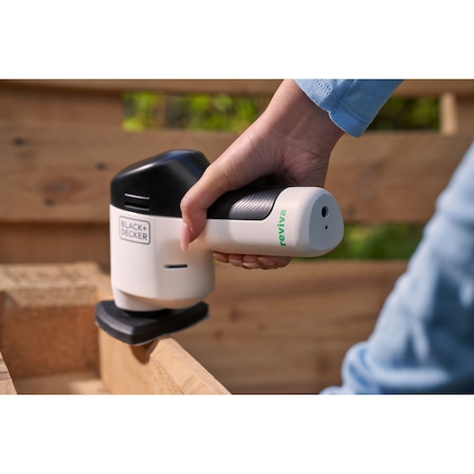 BLACK+DECKER REVDS12C cordless detail sander in use on wood corner, black and white, handheld.