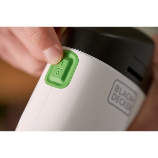 Close-up photo of a hand pressing green power button on BLACK+DECKER REVDS12C appliance, logo visible.