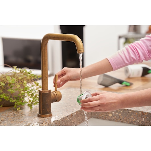 BLACKDECKER REVHV8C handheld vacuum filter being rinsed under kitchen faucet, close-up photography.