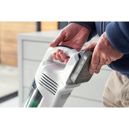 Close-up of hands attaching battery to BLACKDECKER REVSV18D1 cordless vacuum cleaner indoors.