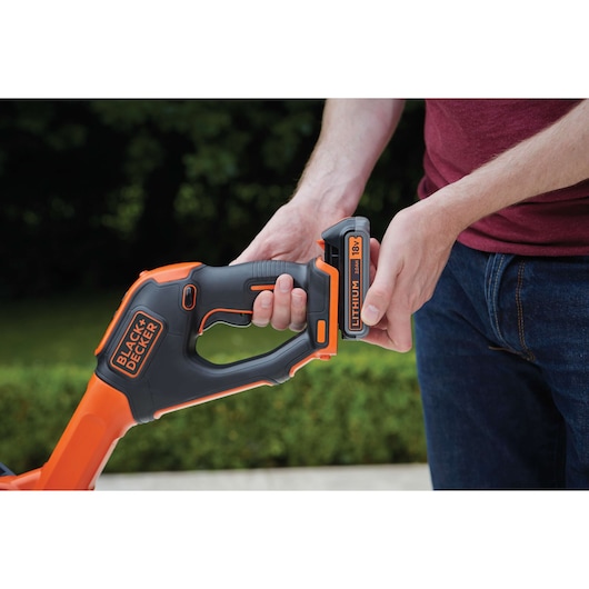 Close-up of BLACK+DECKER STC1820PCB garden tool handle with user inserting 18V lithium battery outdoors.