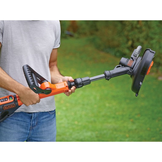 Photo of person holding BLACKDECKER STC1820PC cordless grass trimmer, orange and black, in a garden.