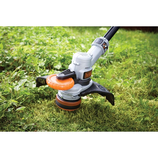 A close-up view of a BLACK+DECKER grass trimmer being used to cut grass and weeds outdoors.