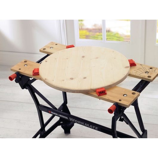 BLACKDECKER WM626 workbench holding round wooden board with red clamps, indoor setting.